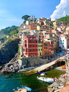 boats are parked on the shore in front of colorful buildings and people walking around them