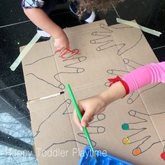 two children playing with construction paper and pencils in front of a cardboard box on the floor