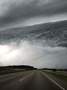 an image of a storm coming in from the sky over a road that is lined with grass and trees