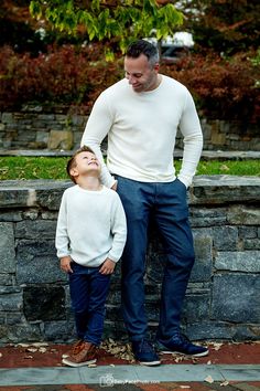 a man standing next to a little boy in front of a stone wall with his eyes closed