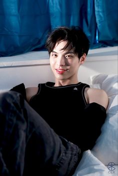 a young man sitting on top of a bed next to a blue curtained window