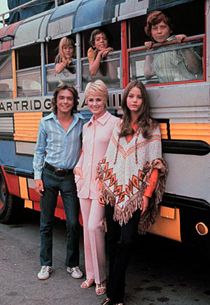 two women and a man standing in front of a bus with people on the side