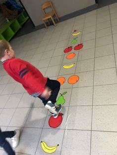 a little boy standing on top of a white tiled floor next to an apple and banana line