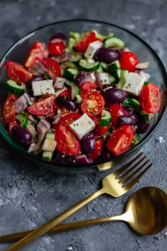 a salad with cucumbers, tomatoes, olives and feta cheese in a glass bowl