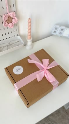 a brown box with pink ribbon on top of a white table next to a candle