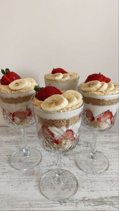 four desserts with strawberries and banana slices in small glass dishes on a white wooden table