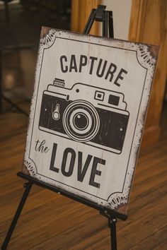 a sign that says capture the love with a camera on it in front of a wooden floor