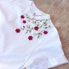 a white t - shirt with red flowers and green leaves embroidered on the chestline