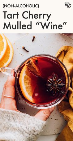 a person holding a glass of mulled wine with an orange slice on the side