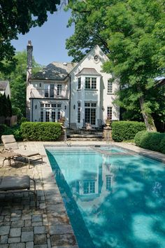 a large white house with a pool in the front yard and lawn chairs around it