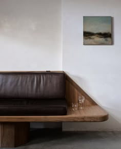 a brown leather couch sitting on top of a wooden table next to a painting and two wine glasses