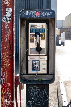 an old fashioned pay phone with graffiti all over it's sides and the telephone is plugged in