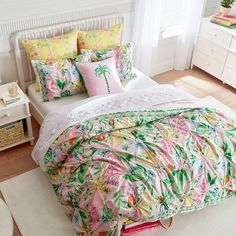 a bed with pink and green comforters in a bedroom next to a white dresser