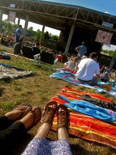 two people sitting on the grass with their feet propped up in front of an open air stage