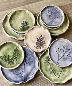 four plates with plants painted on them sitting on a wooden table next to each other