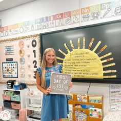 a girl holding up a sign in front of a blackboard with the first day of school written on it