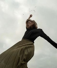 a woman flying a kite in the air with her arms stretched out to catch it