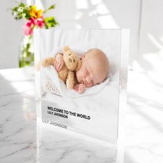 a baby is laying down with a teddy bear in his lap and welcome to the world card