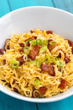 a white bowl filled with noodles and bacon on top of a blue wooden table next to a fork