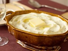 a wooden bowl filled with mashed potatoes next to a glass of wine