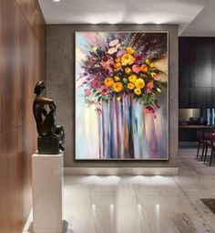 a painting hanging on the wall above a vase filled with flowers in front of a dining room table