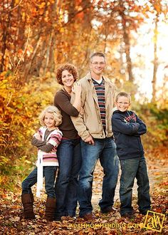 a family posing for a photo in the woods with autumn leaves on the ground and trees behind them