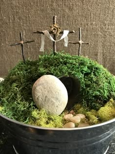 a bucket filled with moss and rocks on top of a table next to a cross