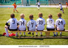 a group of young boys sitting on top of a bench in front of a soccer field