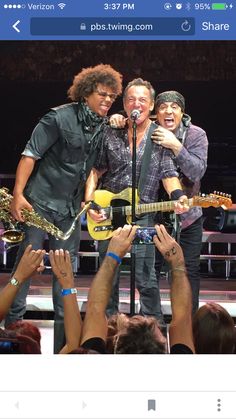 two men standing on stage with guitars and microphones in front of them while people are taking pictures