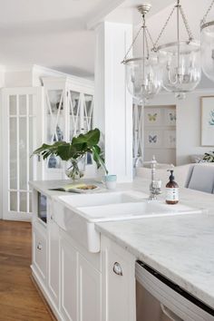 a white kitchen with marble counter tops and an island in front of the sink is surrounded by hanging glass chandeliers