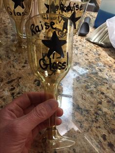 someone is holding up two wine glasses with black stars on the bottom and one has a name written on it