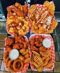 four baskets filled with different types of fried food on top of each other and dipping sauce in the middle