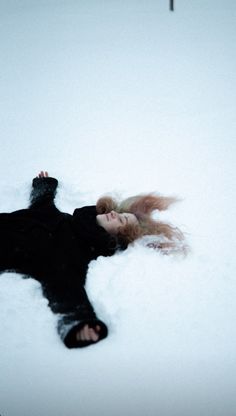 a woman laying in the snow with her hair blowing