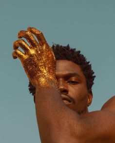 a man with his hands in the air and gold paint on his face, wearing gloves