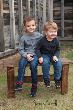 two young boys sitting on top of a wooden bench