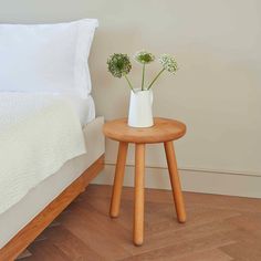 a small wooden table with two flowers on it in front of a bed and nightstand