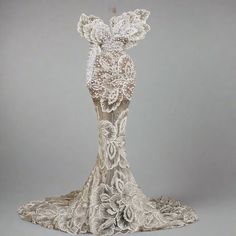 an intricately designed dress is displayed on a gray surface with white flowers and leaves