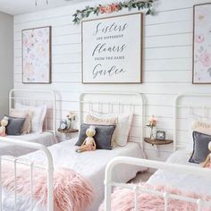 two white beds in a room with pink fluffy pillows on them and pictures above the beds