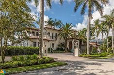 a large white house with palm trees in the front yard and landscaping on both sides