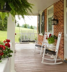 two white rocking chairs sitting on a porch next to flowers and potted planters