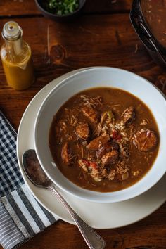 a white bowl filled with meat and vegetable soup next to a glass of orange juice