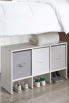 a bed with white sheets and shoes on the bottom shelf next to each other in front of it