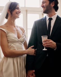 a bride and groom standing next to each other in front of a window holding champagne glasses