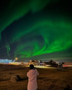 a person standing in front of an aurora bore with green lights on the night sky