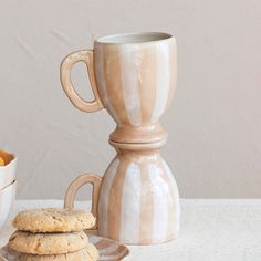 two cookies are on a plate next to a coffee pot and bowl with oranges in it