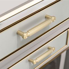 a white and gold dresser with two drawers on each side, one drawer has brass handles