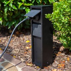 a black device is plugged into the ground in front of some bushes and trees