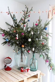 a christmas tree sitting on top of a wooden table next to two vases filled with ornaments