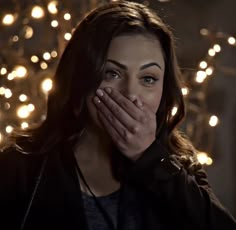 a woman covering her mouth in front of a string of christmas lights on the wall