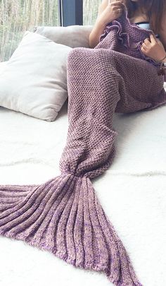 a woman laying on top of a bed next to a purple knitted mermaid tail